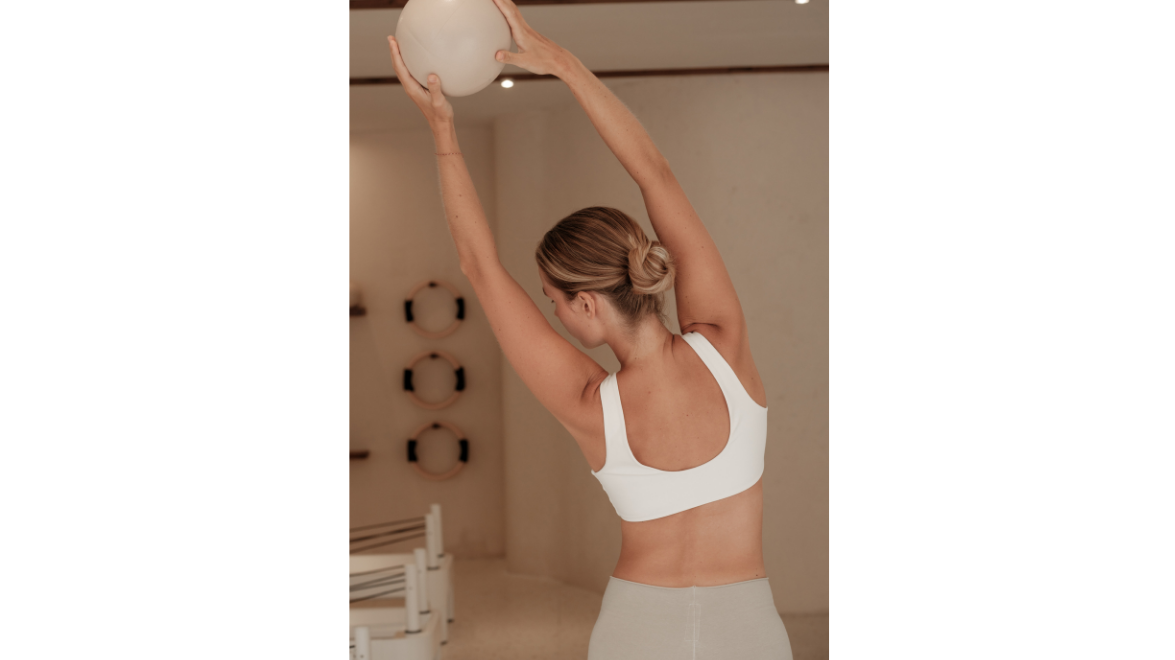 Woman training with a stability ball in a gym, arms extended overhead