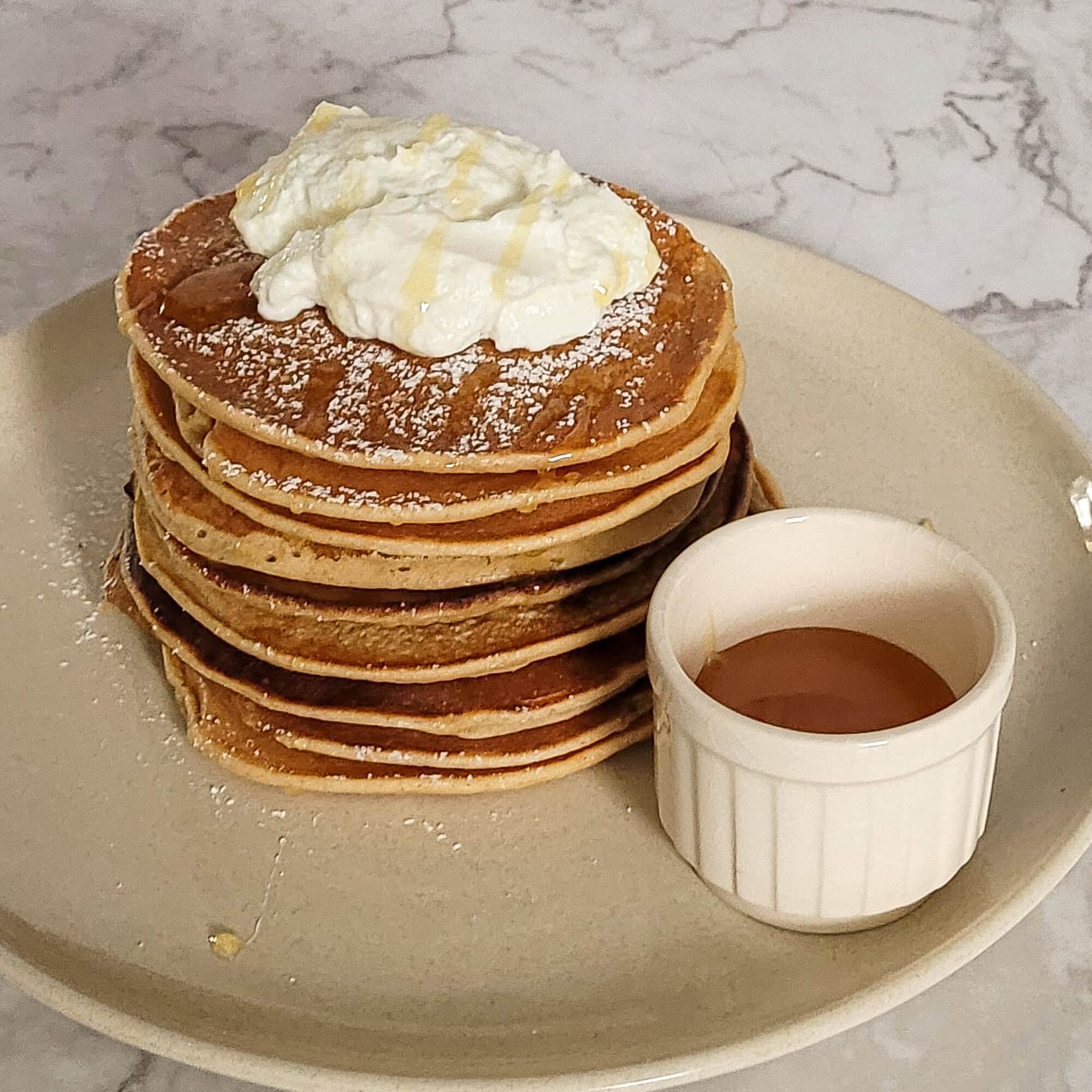Stack of whole wheat banana pancakes with whipped cream and syrup on a plate.