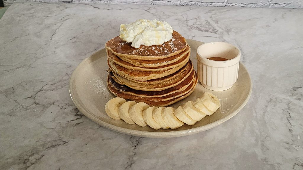 Stack of whole wheat banana pancakes with banana slices and syrup.