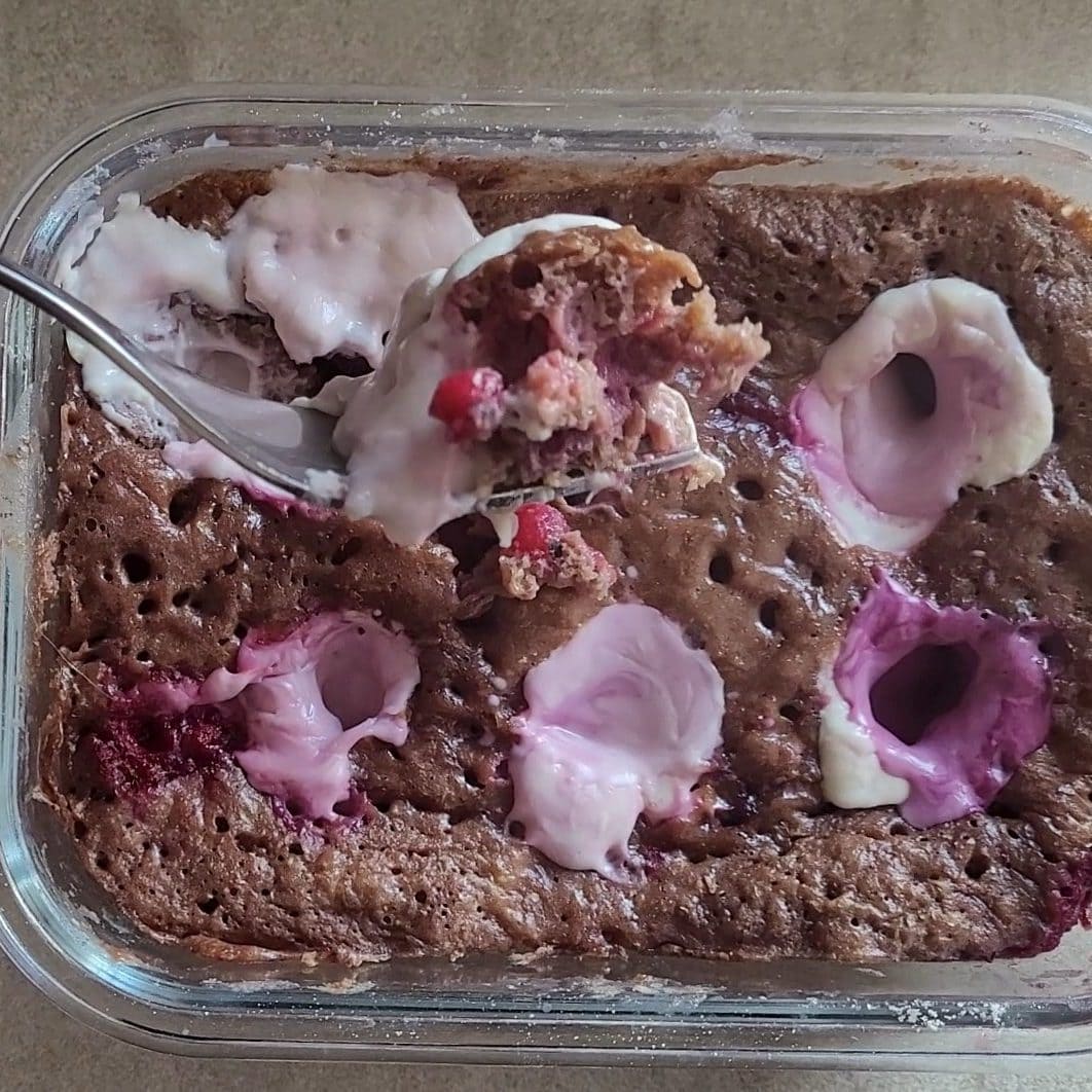Close-up of a microwave cheesecake in a glass bowl with pink and white toppings.