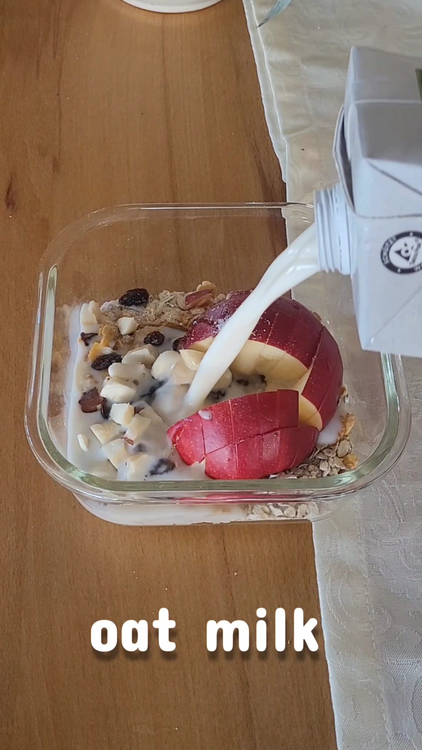 Microwave apple oatmeal with oat milk being poured over oats and apple pieces in a bowl before cooking.