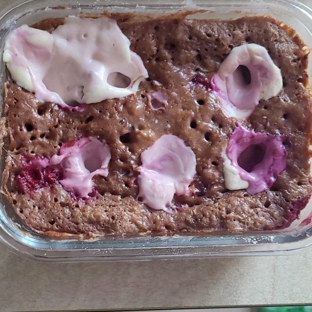 Close-up of a microwave cheesecake with chocolate in a glass bowl with pink and white toppings.