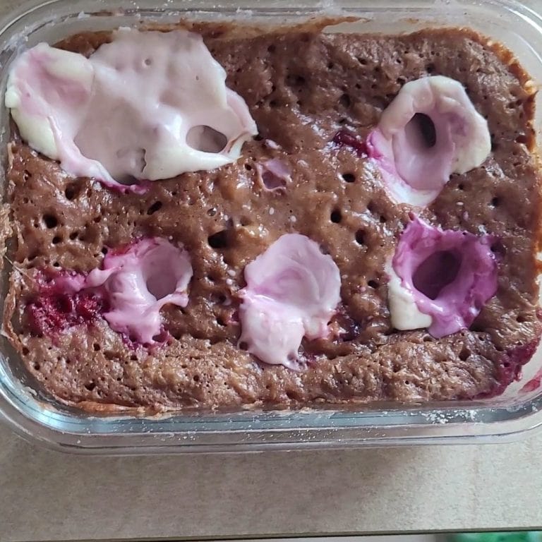 Close-up of a microwave cheesecake with chocolate in a glass bowl with pink and white toppings.