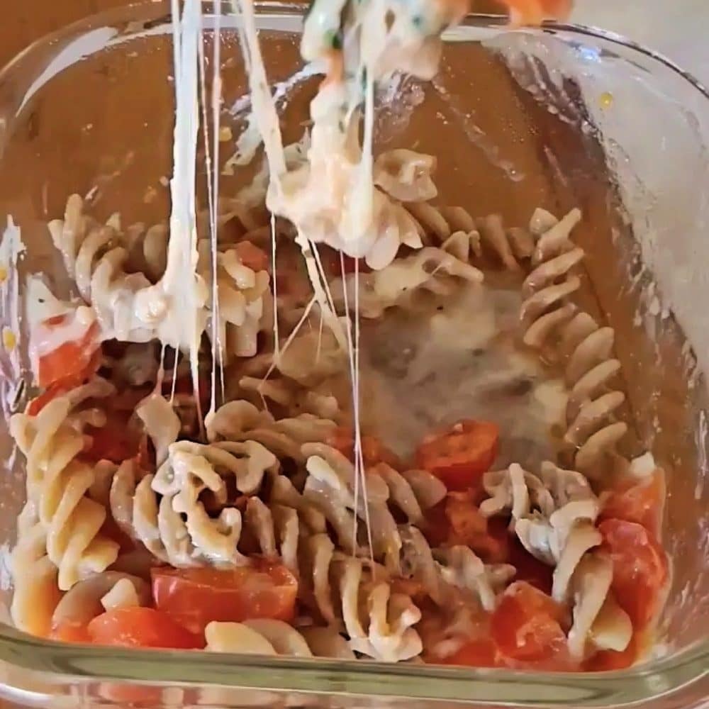 Mixing leftover pasta with tomatoes, cheese and seasoning in a bowl before microwaving