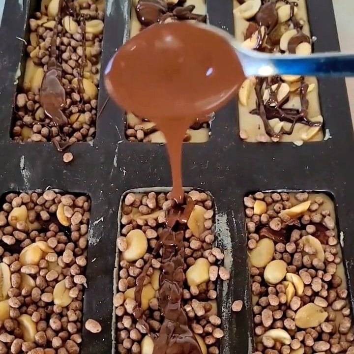 Chocolate poured over homemade protein bars with peanuts and crunchy toppings