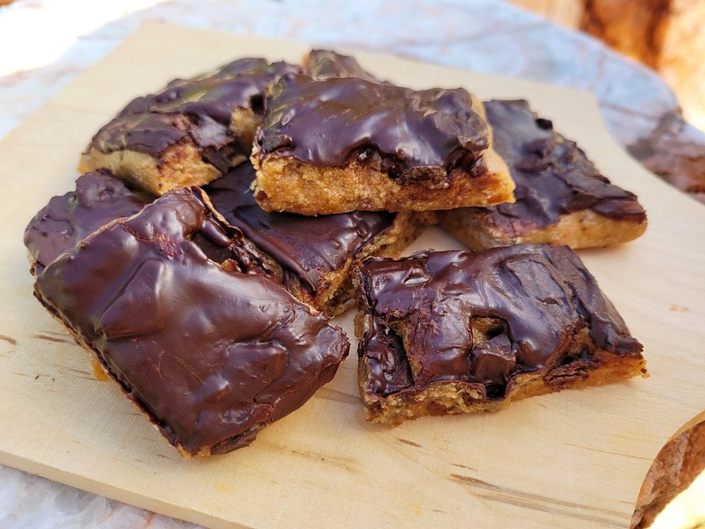 Homemade date protein bar recipe with soft fudgy center and dark chocolate topping cut into squares on wooden board