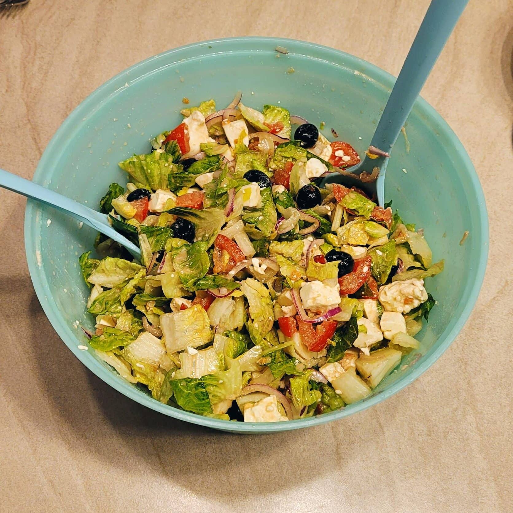 Healthy Greek salad with feta, mozzarella, and fresh vegetables in a blue bowl.