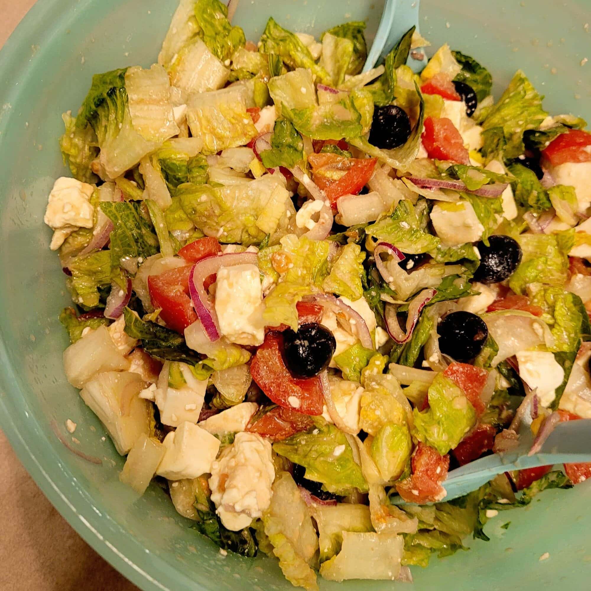 Healthy Greek salad with feta, mozzarella, and fresh vegetables in a blue bowl.