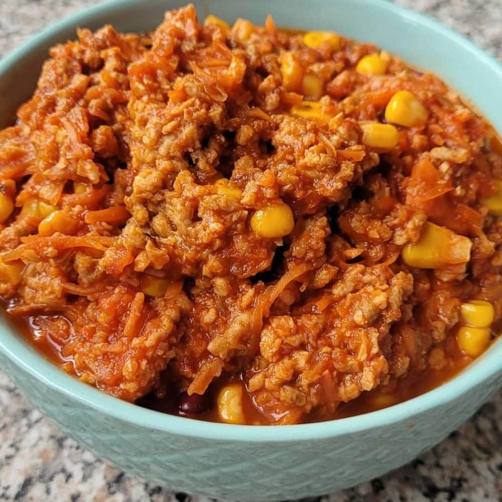Bean chili in a blue bowl, top view showing vegan ground meat, kidney beans, corn, and tomato based sauce