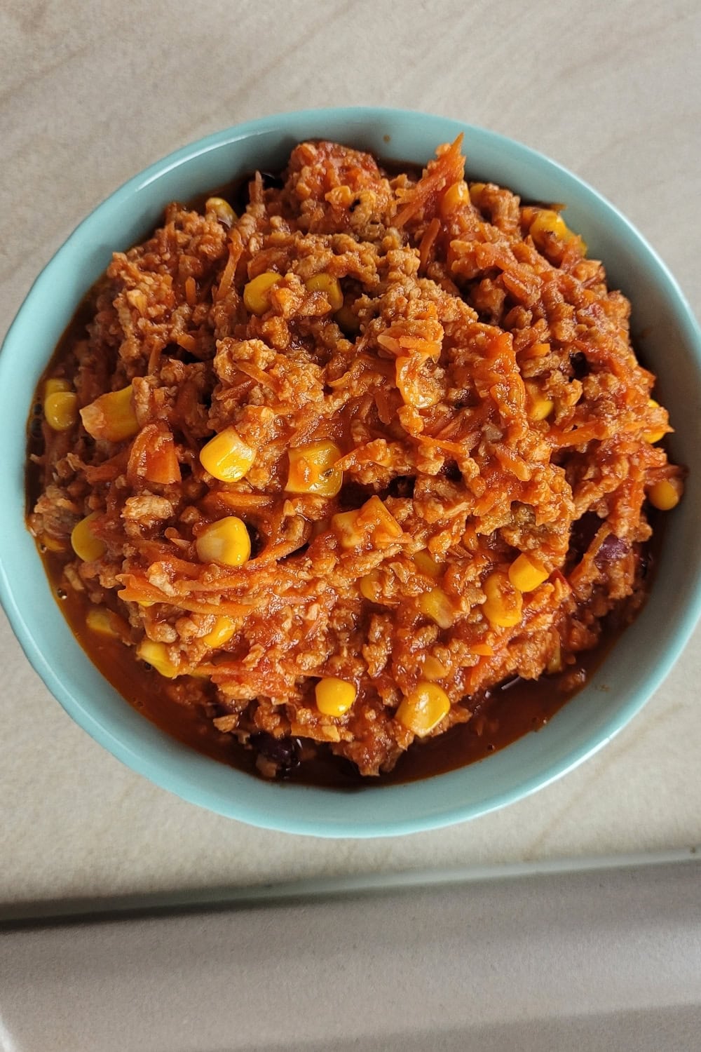Bean chili in a blue bowl, top view showing vegan ground meat, kidney beans, corn, and tomato based sauce