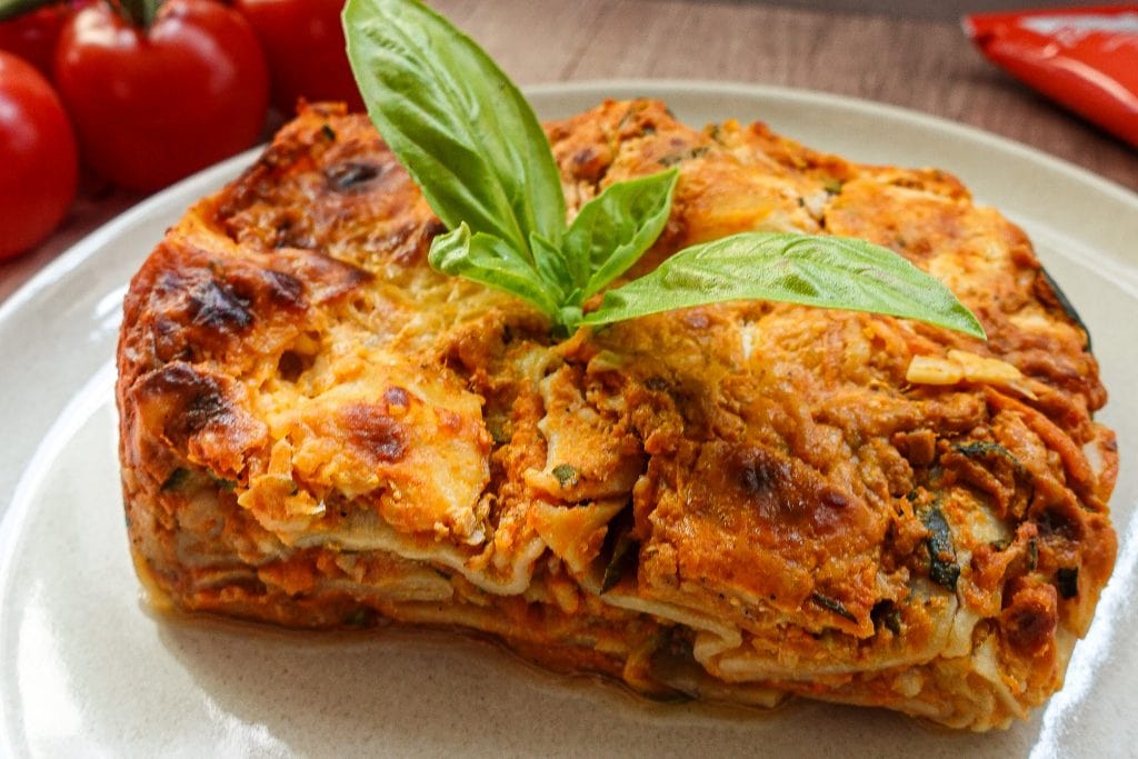 Delicious vegetable lasagna with fresh basil on top, on a plate next to tomatoes