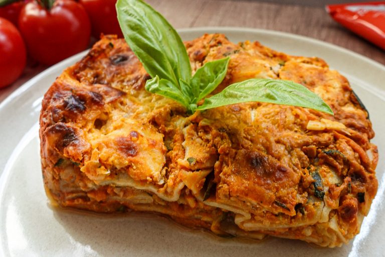 Delicious vegetarian lasagna slice garnished with basil on a white plate.