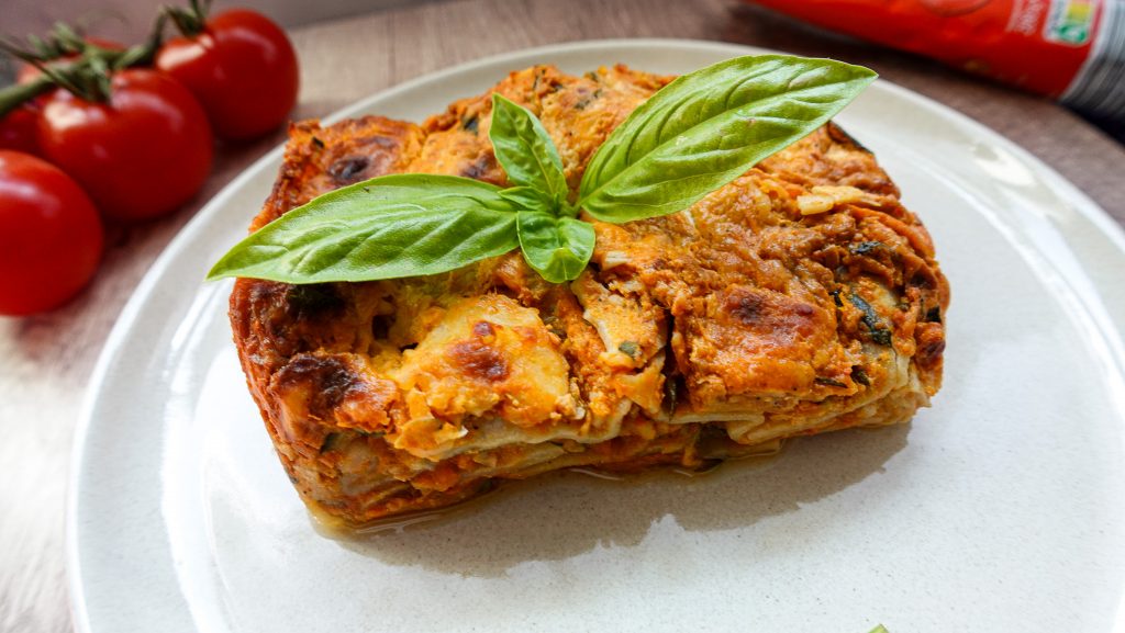 Close-up of a vegetarian lasagna slice garnished with basil on a white plate.