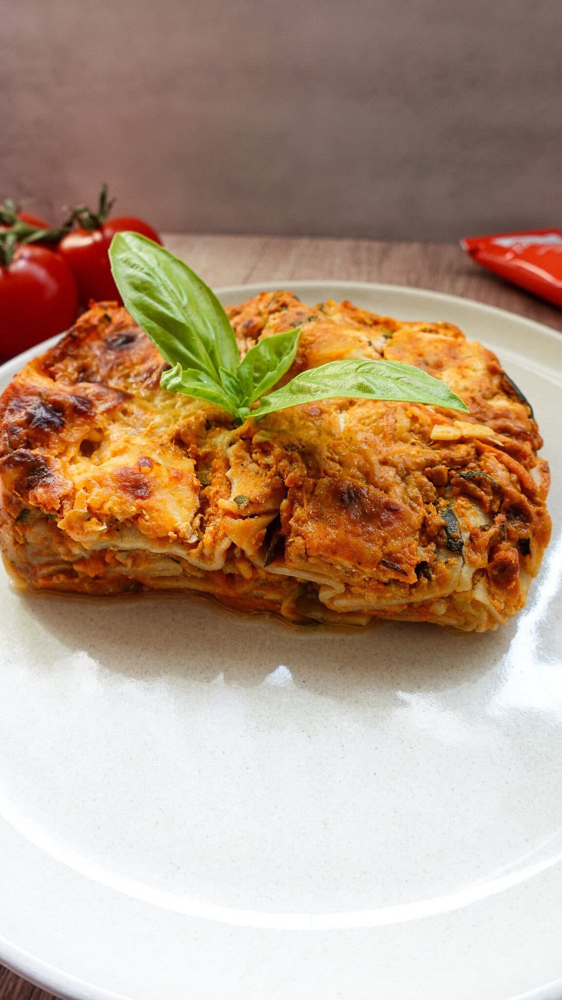 Delicious vegetarian lasagna with fresh basil on top, served on a white plate.