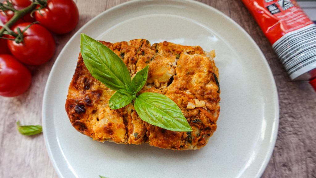 the best vegetable lasagna decorated with fresh basil on top, on a white plate