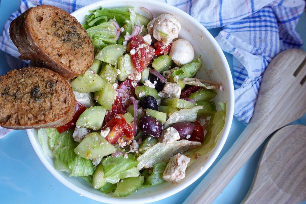 Fresh Greek salad with feta, mozzarella, cucumbers, and tomatoes in a white bowl.
