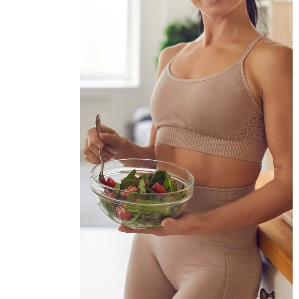 Woman in activewear preparing a fresh salad in a kitchen