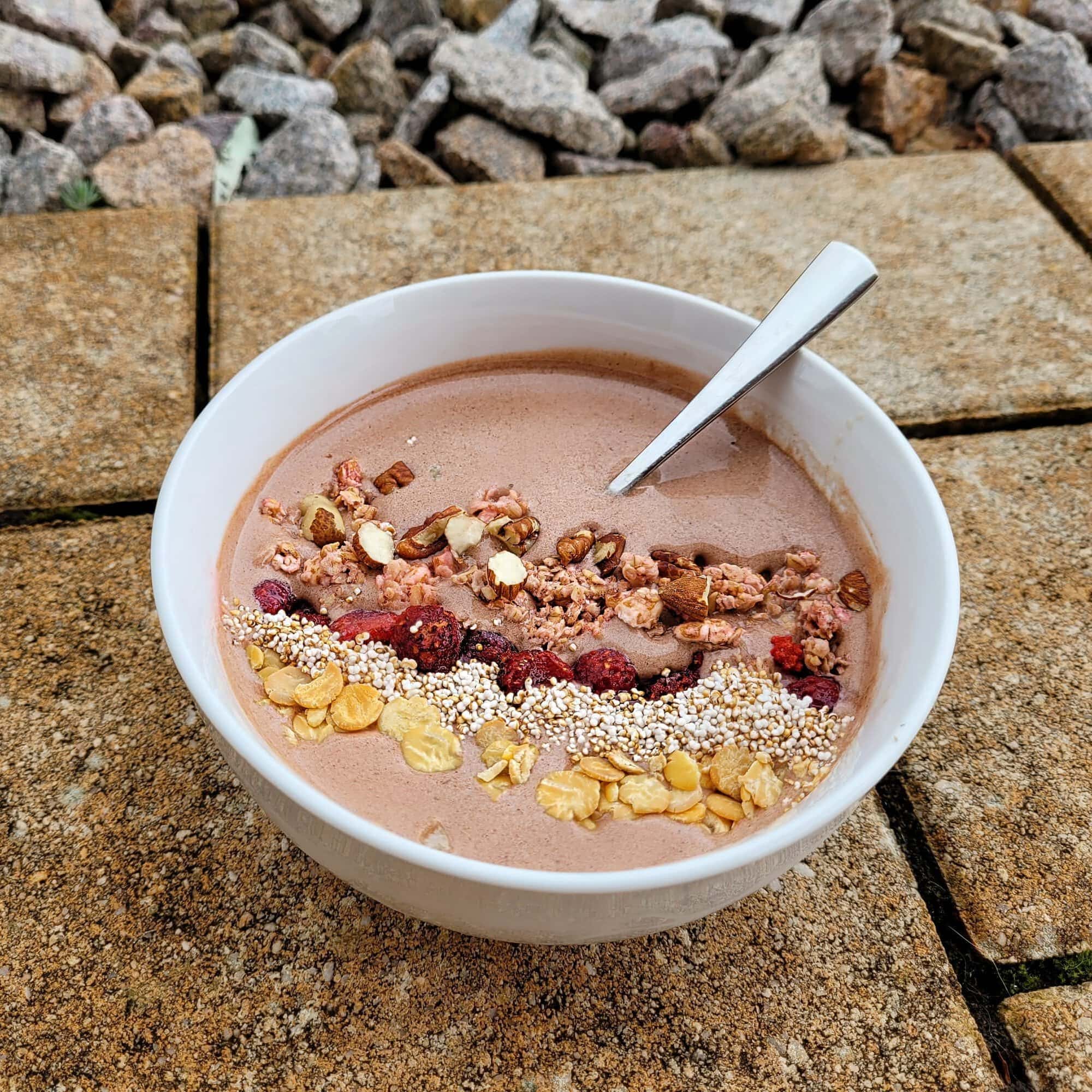 High protein chocolate smoothie bowl with raspberries, crunchy granola, and mixed nuts on top