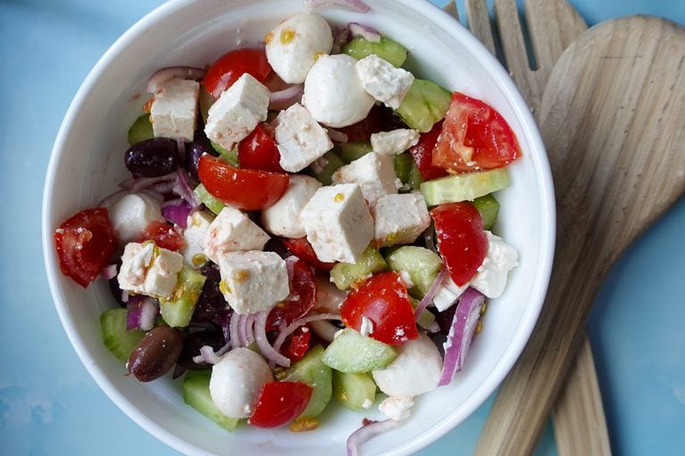 Colorful Greek salad with feta, cherry tomatoes, cucumbers, and olives in a white bowl.