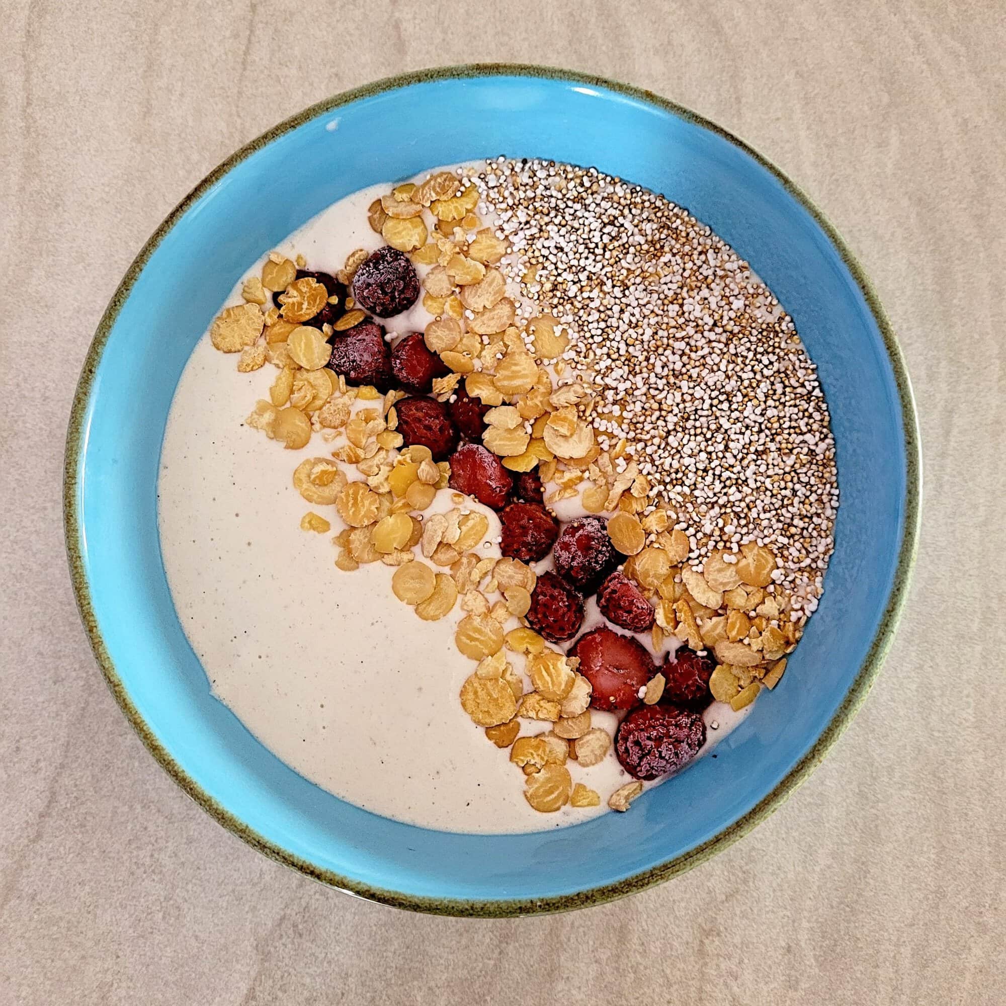 vanilla smoothie bowl side by side topped with raspberries, granola, and nuts in ceramic bowls