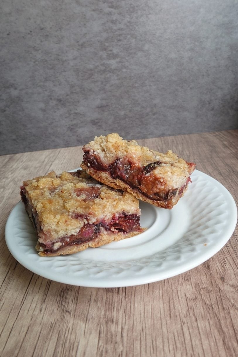 Soft German plum cake bars with golden crumble topping and baked fresh plums on a ceramic plate