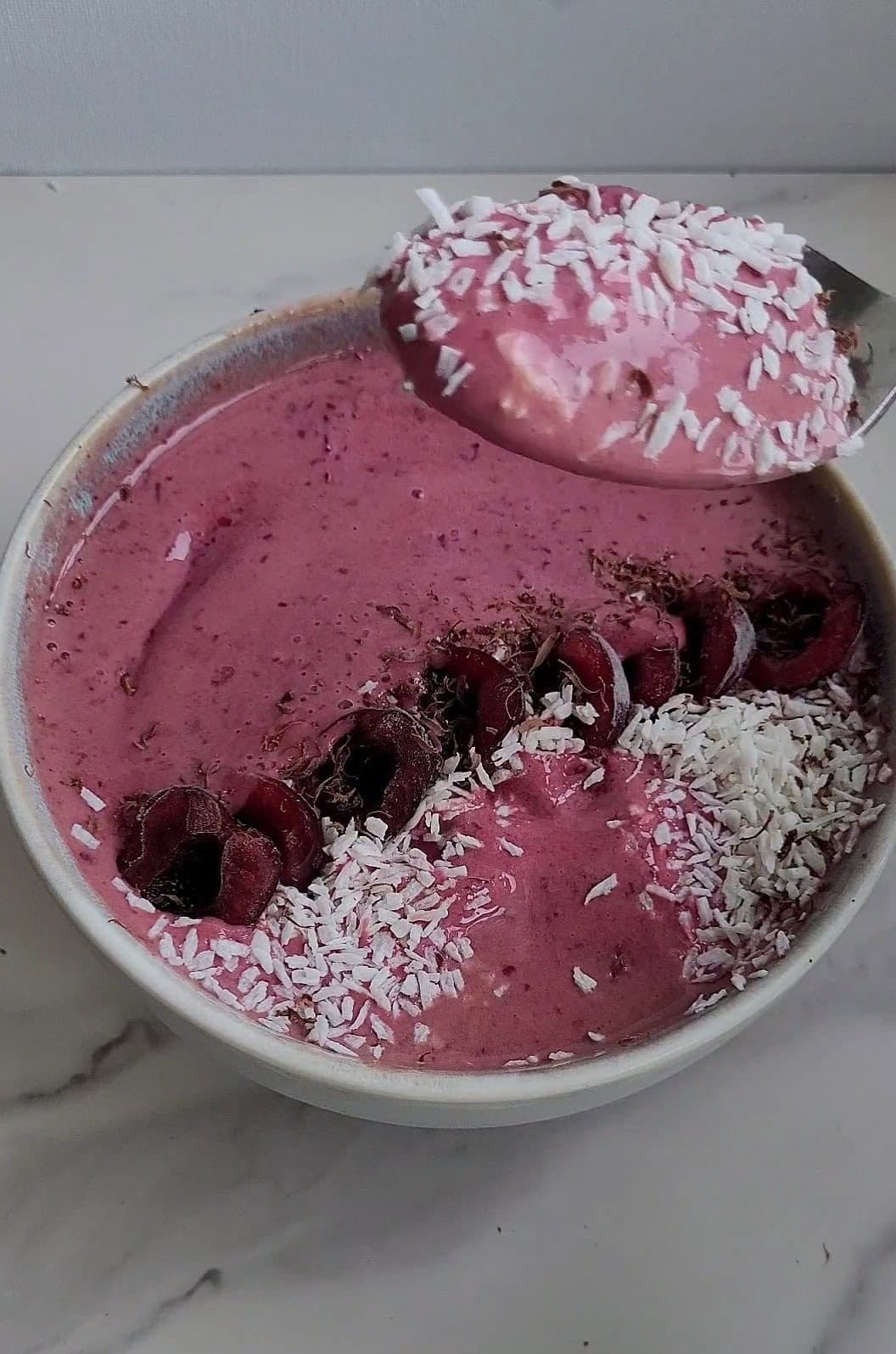 Delicious pink berry smoothie topped with coconut flakes and cherries.