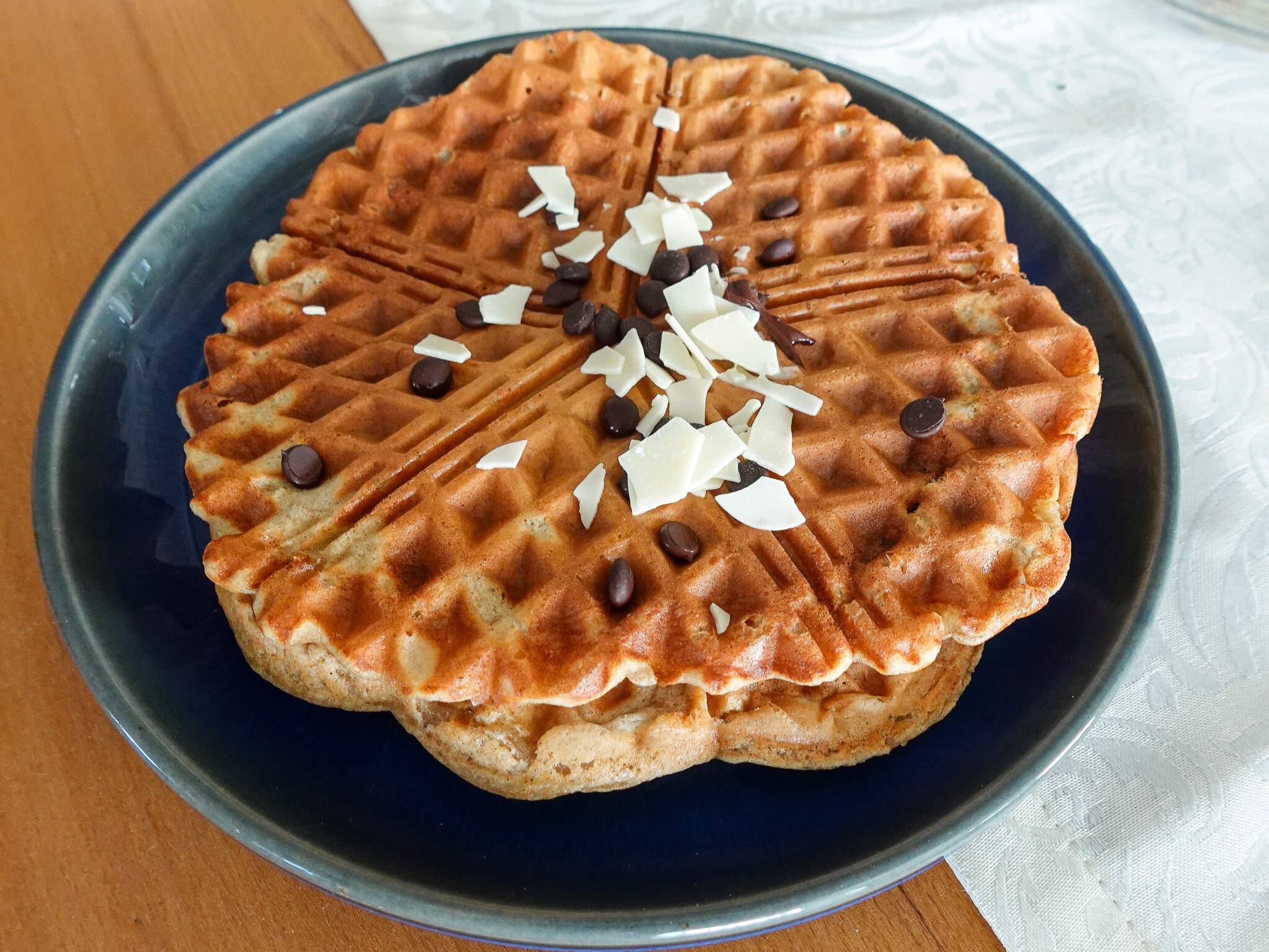 Healthy banana waffle recipe topped with chocolate chips and white chocolate on a blue plate.