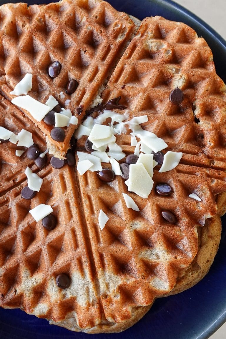 Close-up of banana waffles topped with chocolate chips and white chocolate shavings.