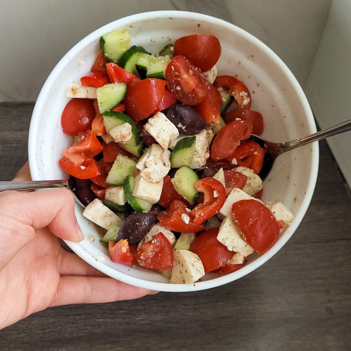 Colorful Greek salad with tomatoes, cucumbers, feta cheese, and olives in a white bowl.