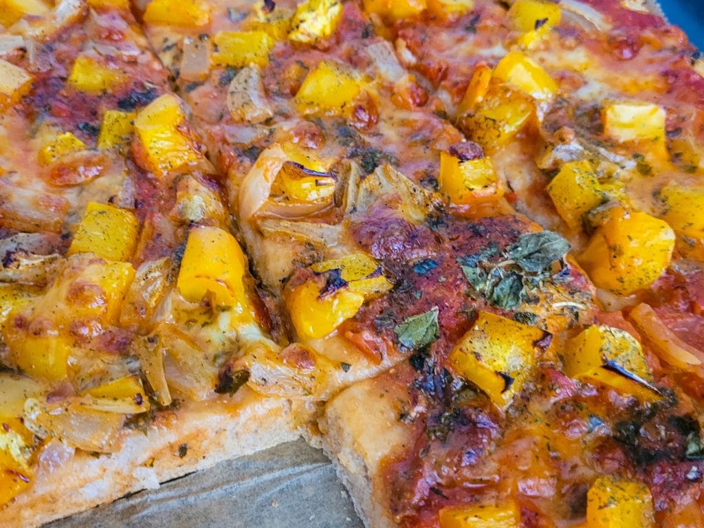 Close-up of a pizza topped with yellow squash, onions, and herbs.