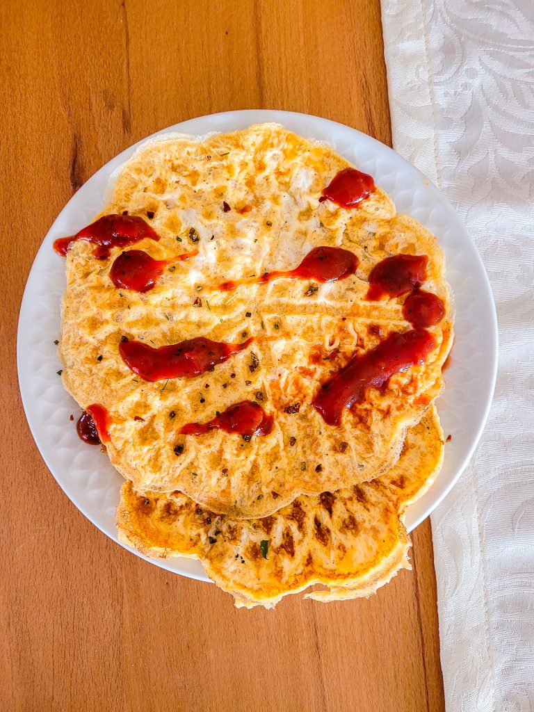 Two crispy egg waffles topped with ketchup on a white plate.