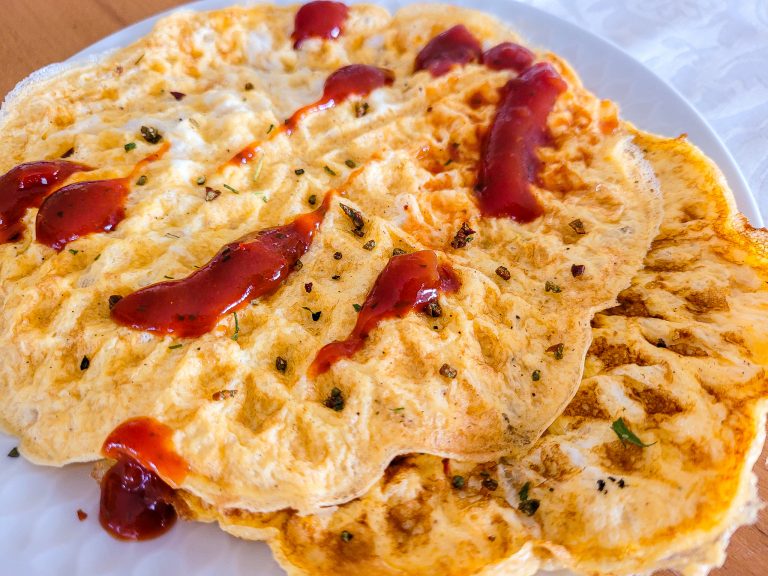 Close-up of a crispy egg waffle with ketchup and herbs.