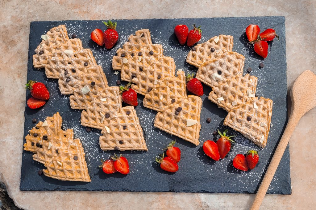 Delicious whole grain waffles on a tray topped with fresh strawberries and chocolate chips.