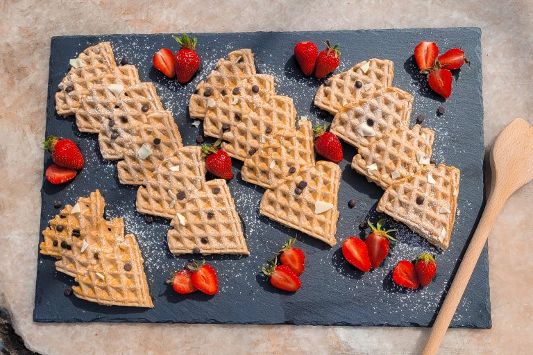 Whole grain waffles with fresh strawberries on a black slate serving board.