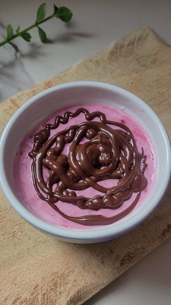 Top view of a healthy raspberry Greek yogurt dessert topped with dark chocolate.