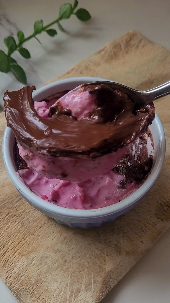 Greek yogurt dessert with raspberry compote and dark chocolate in a glass with a spoon.