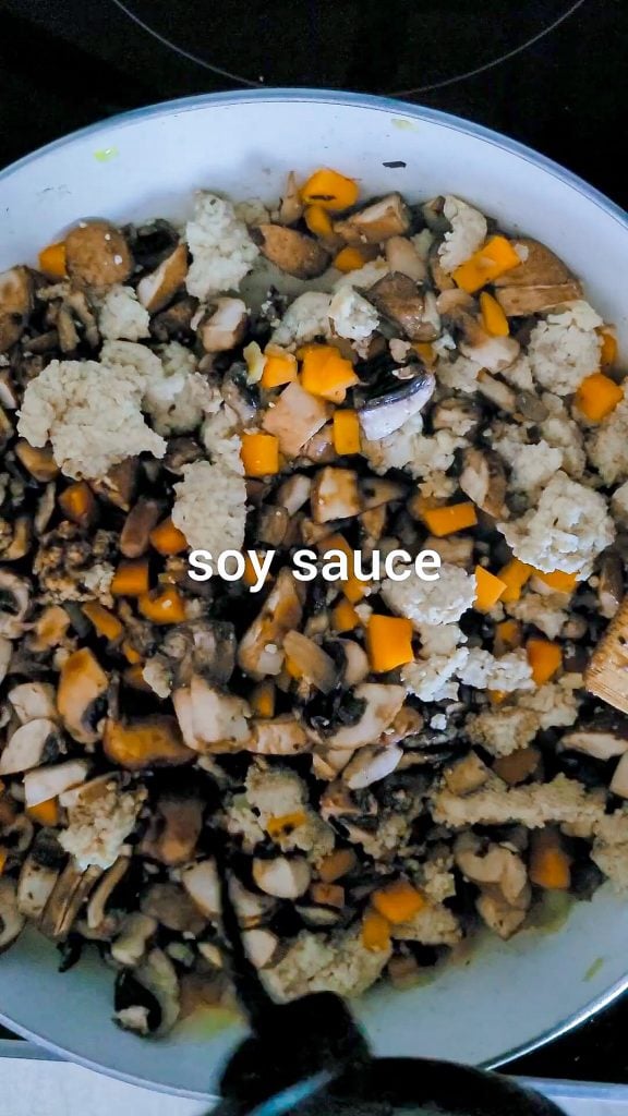 mushrooms mixed with carrots and tofu in a pan. Adding soy sauce