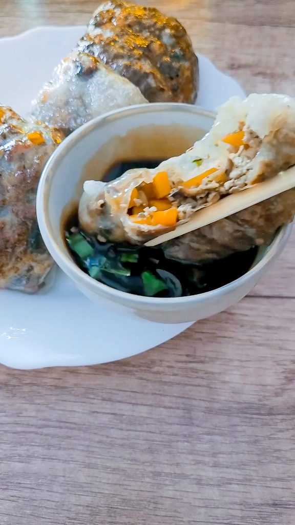 Close-up of stuffed dumpling with vegetables and tofu on a wooden table.