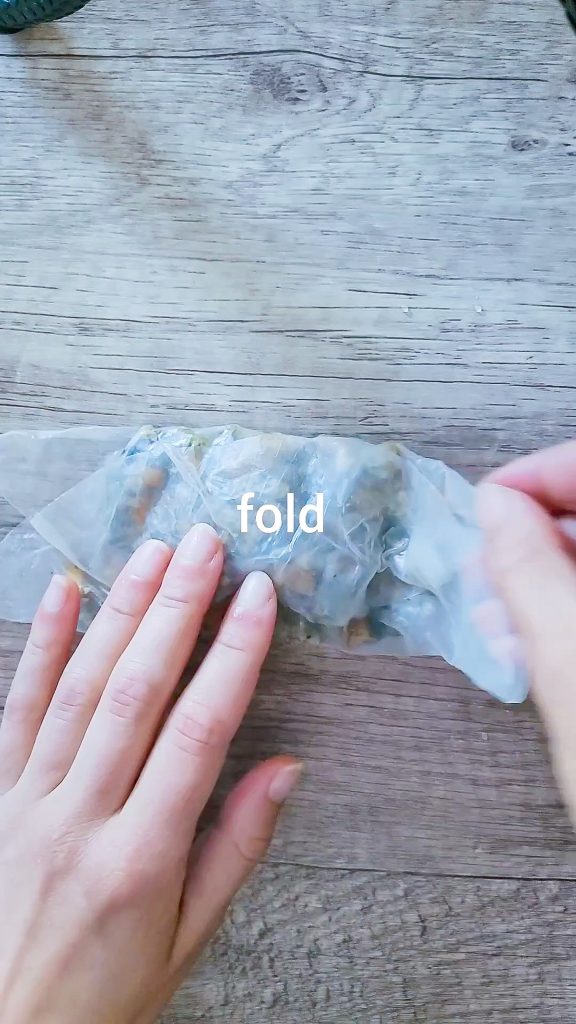 picture showing how to fold the dumpling by having the filling in the center of the wet rice paper. The upper and lower side  of the paper is folded in and  the sides are folded into the middle as well creating a square like shape. 