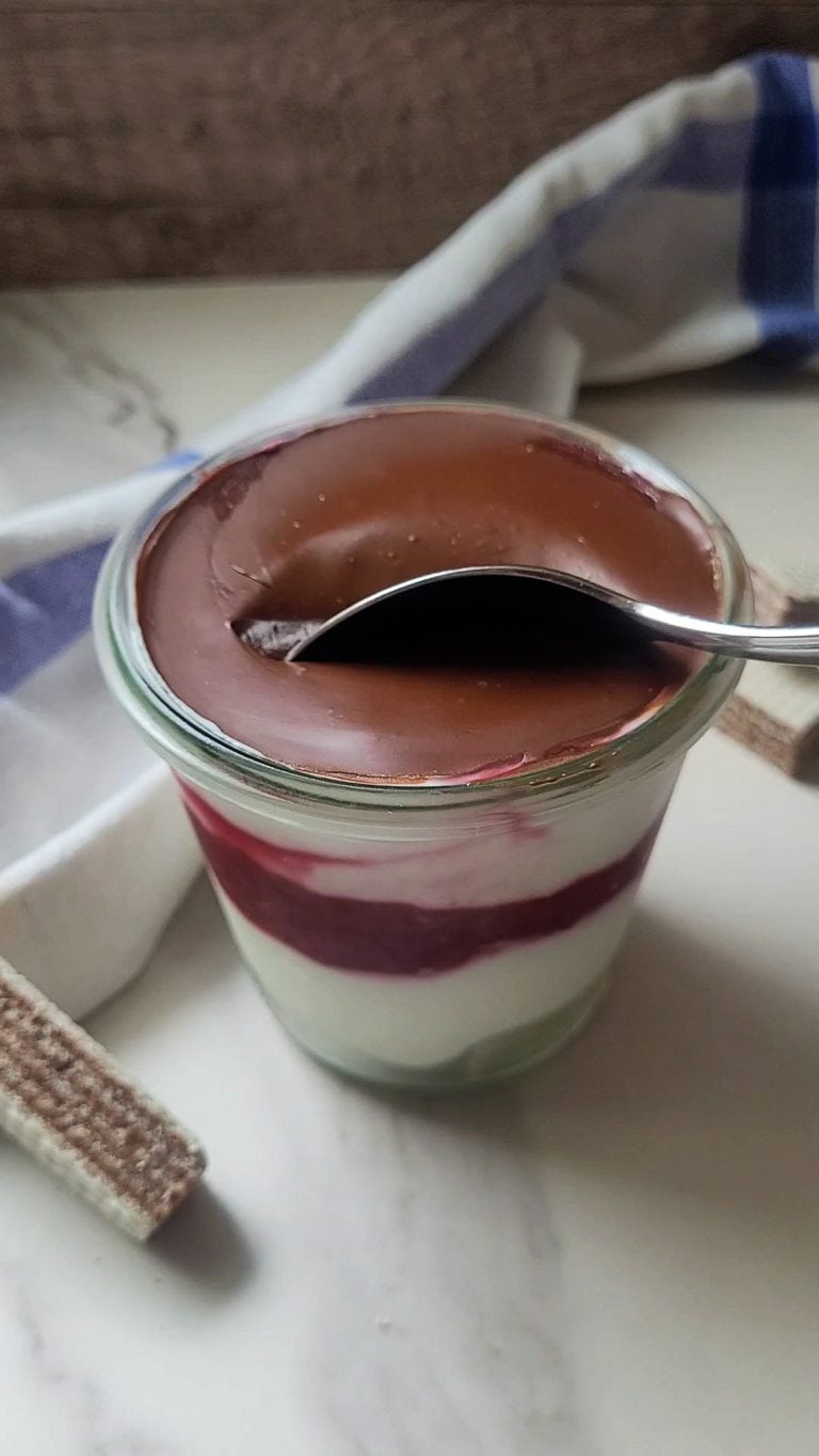 Layered raspberry and Greek yogurt dessert with chocolate topping in a glass jar.