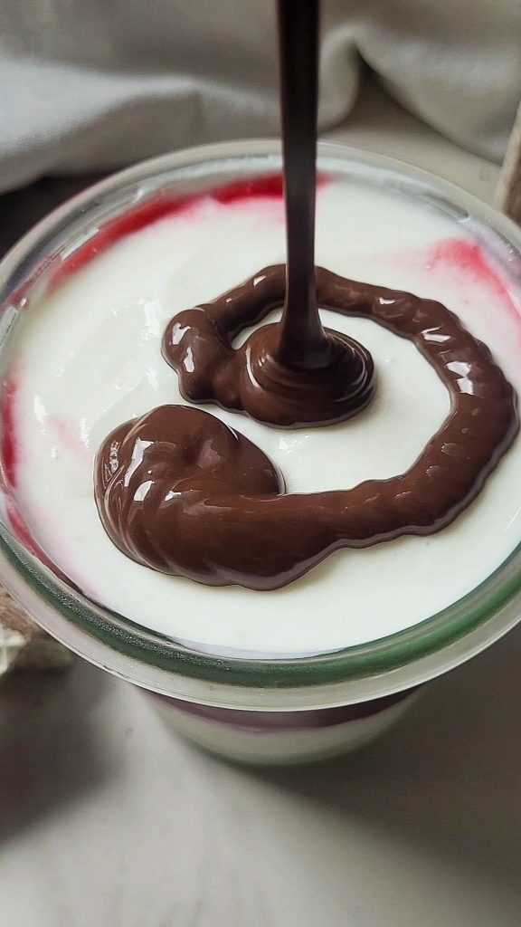 Creamy raspberry dessert with chocolate drizzle in a glass.