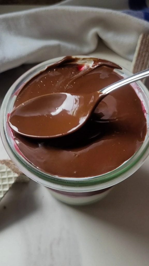 Creamy chocolate and raspberry dessert in glass jar with spoon.