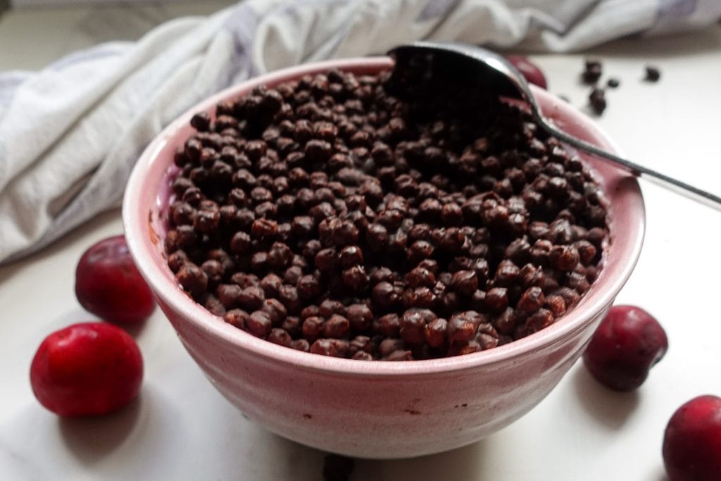 High protein chocolate dessert with magic shell in pink bowl with cherries.