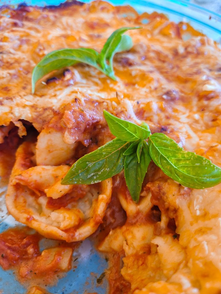 Close-up of creamy tortellini pasta bake garnished with fresh basil leaves.