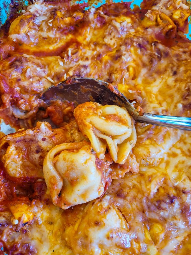 Close-up of cheesy tortellini bake with melted cheese and sauce.