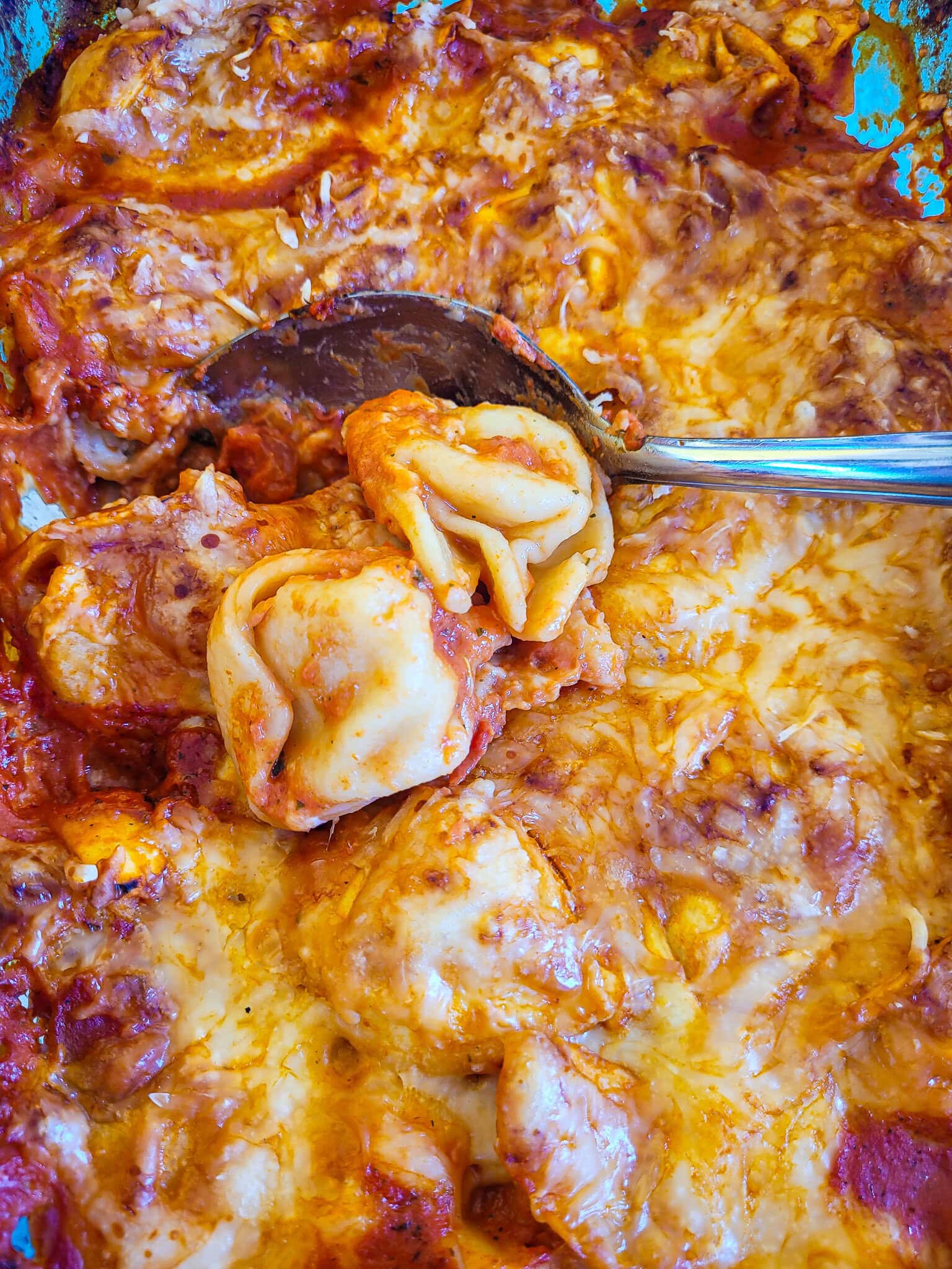 Close-up of cheesy tortellini bake with melted cheese and sauce.