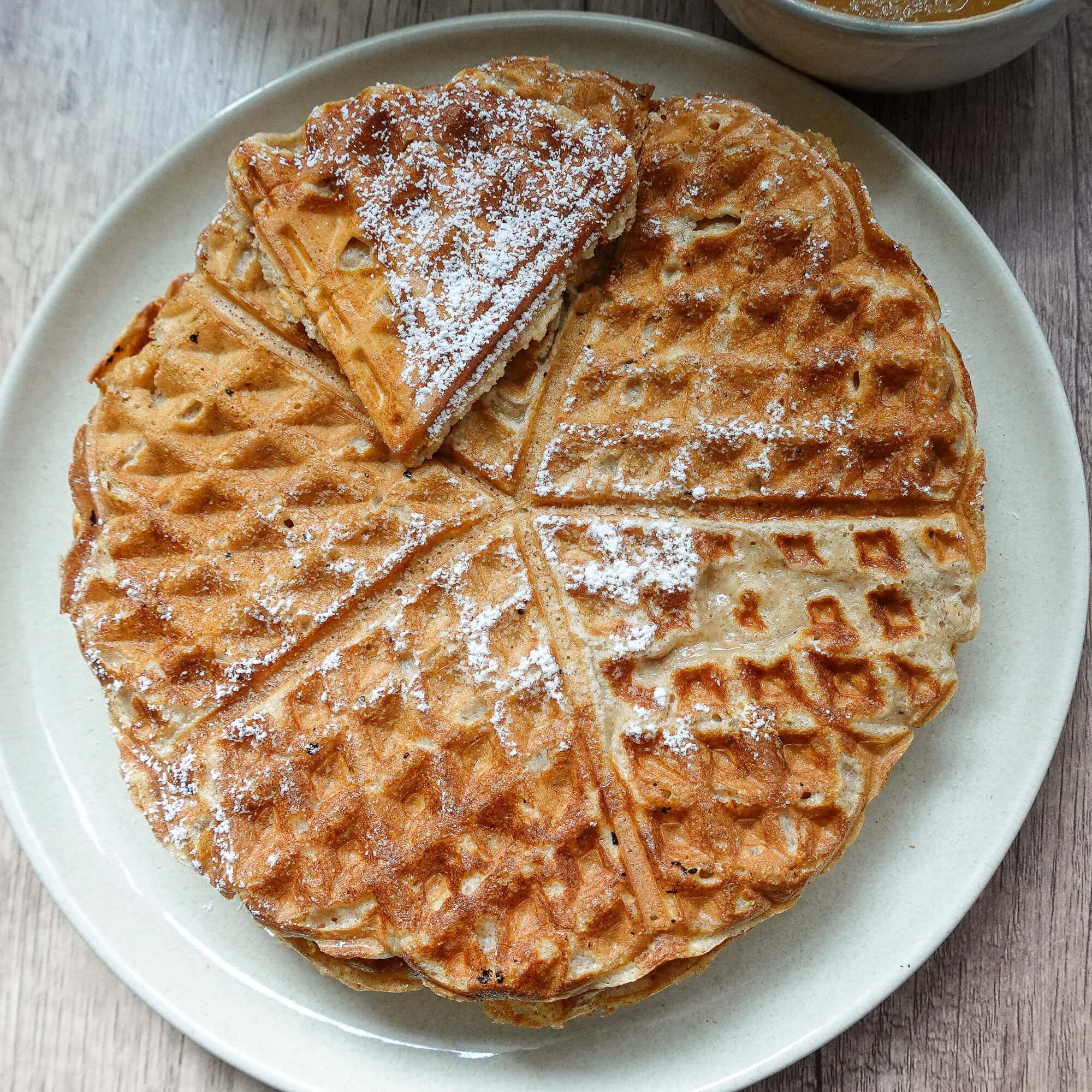 Golden brown apple cinnamon waffles dusted with powdered sugar on a white plate.
