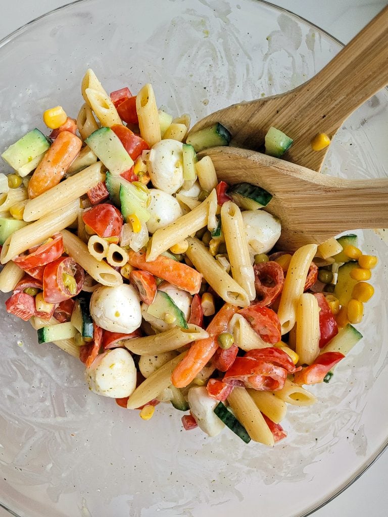 Colorful healthy pasta salad with vegetables and mozzarella cheese in a glass bowl.