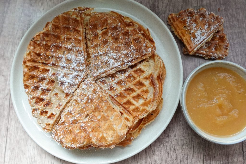 Stack of waffles with powdered sugar and a bowl of applesauce.