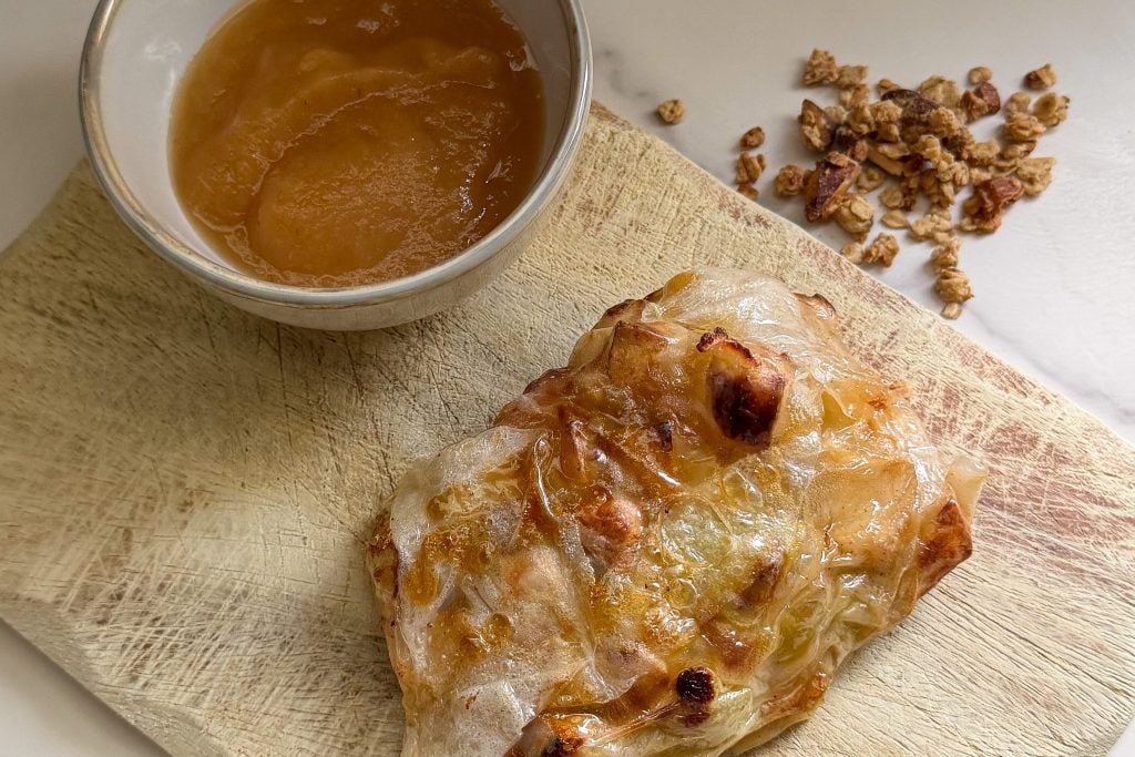 Baked apple with melted cheese and granola on a wooden board.